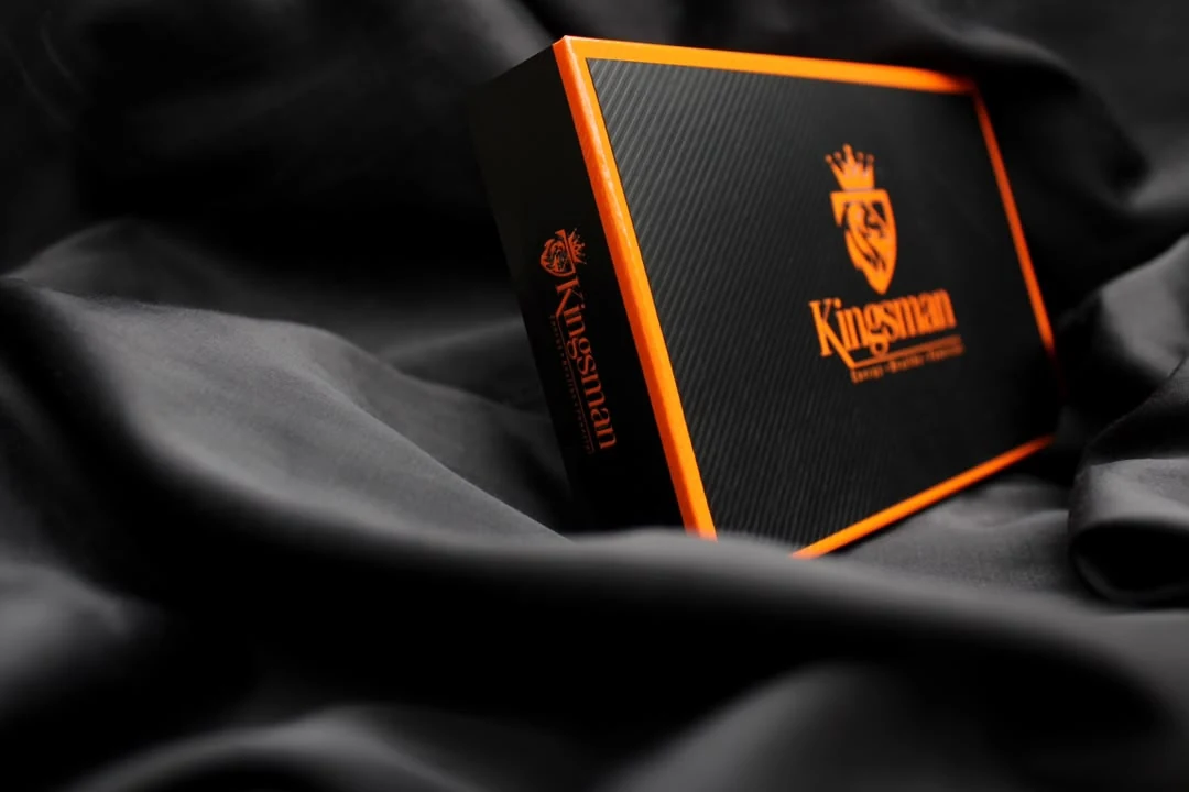 Coffret Kingsman de trois quarts, liseré orange lumineux, sur satin gris